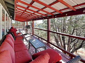 A covered outdoor seating area with red cushioned benches, a grill, and a table. - Nana and Papa's Mountain Retreat by Kokopelli Property Management (Alto)