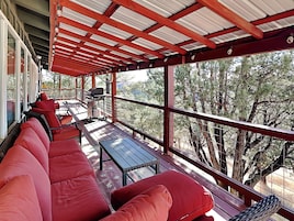 A covered outdoor seating area with red cushioned benches, a grill, and a table.