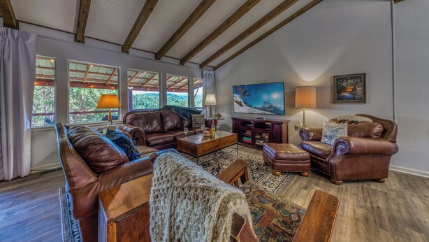 A spacious living room with leather sofas, a wooden coffee table, and a large painting of a mountain scene. - Nana and Papa's Mountain Retreat by Kokopelli Property Management (Alto)