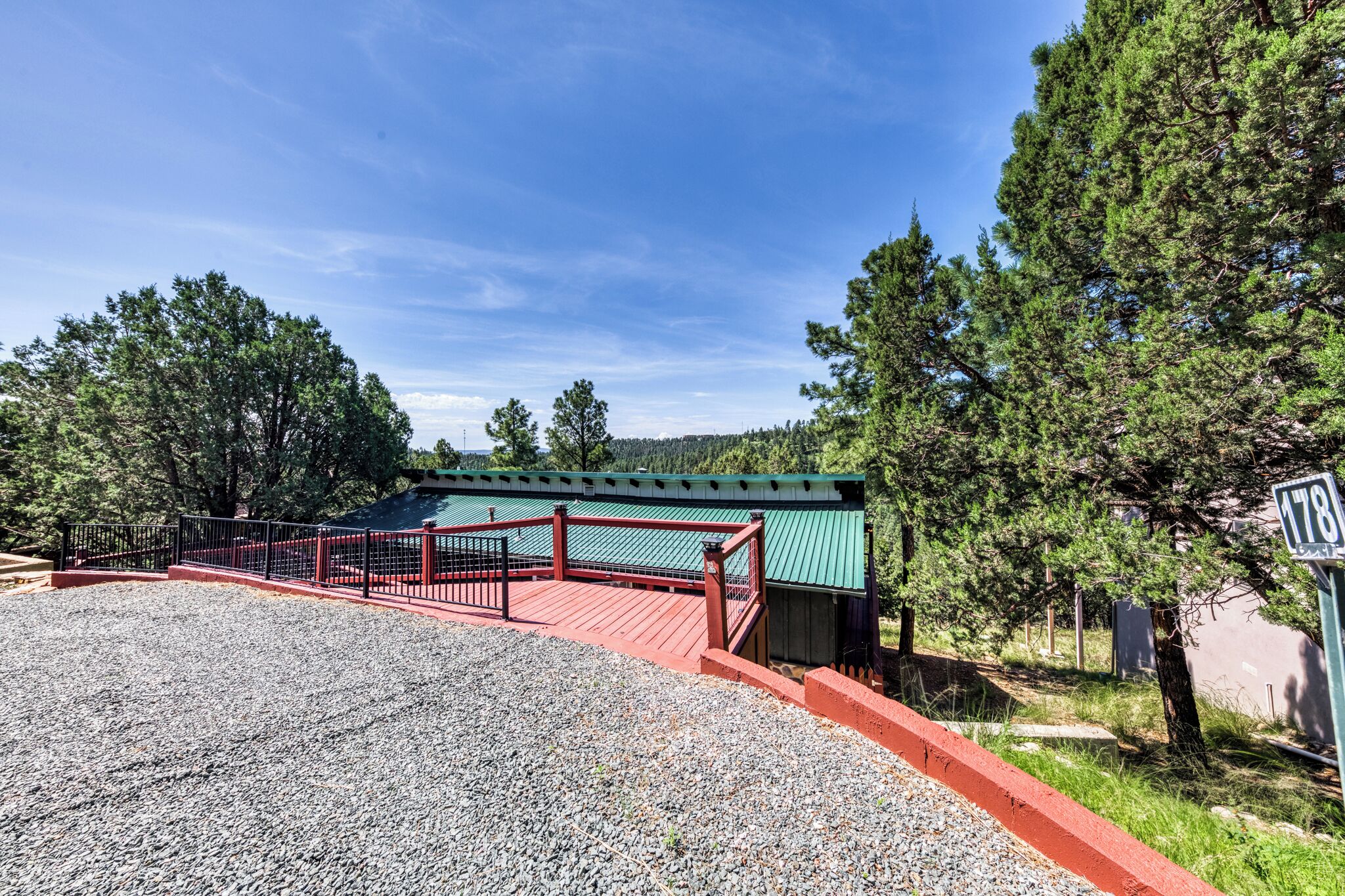 A gravel area with a red and black metal fence leading to a green-roofed building.