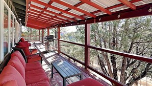A covered outdoor seating area with red cushioned benches, a grill, and a table. - Nana and Papa's Mountain Retreat by Kokopelli Property Management (Alto)