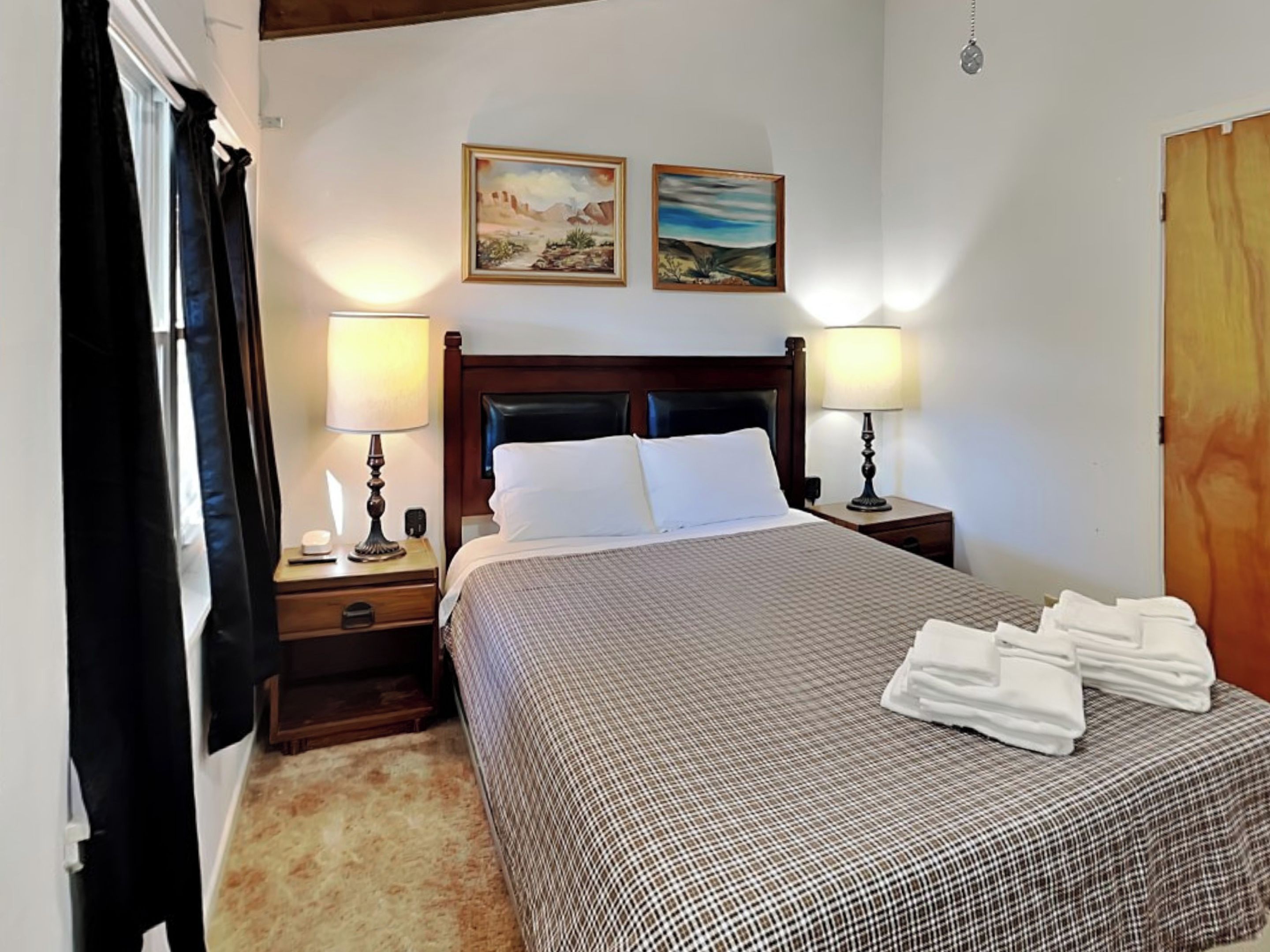 Una camera d'albergo con un letto grande, due lampade ai comodini, una testiera in legno e due quadri alle pareti.