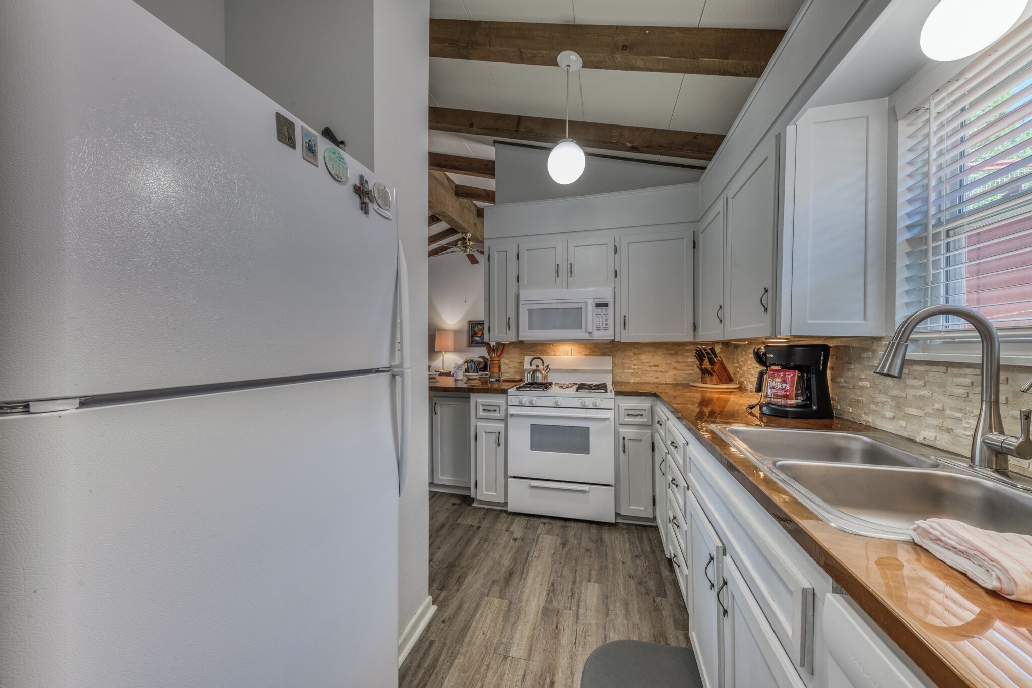 A kitchen with white cabinets, a stainless steel sink, a microwave, and a stove.