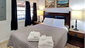 A hotel room with a large bed, two paintings on the wall, a window with curtains, and a nightstand with a lamp. - Nana and Papa's Mountain Retreat by Kokopelli Property Management (Alto)