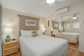 A bedroom with a large bed, two bedside tables, a mirror, and a ceiling fan.