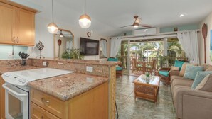 Cucina spaziosa con piani in granito, pensili in legno e forno integrato. È presente una zona pranzo con mobili in vimini e una ventola a soffitto.
