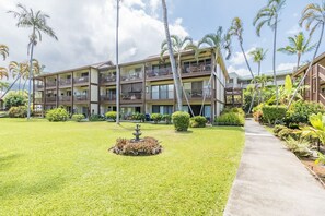 A multi-story hotel with balconies, a central garden with a fountain, and palm trees.