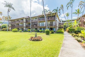 Un hotel de varios pisos con balcones, un jardín central con una fuente y palmeras.
