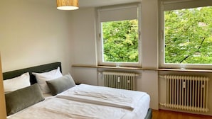 Une chambre à coucher avec un lit, deux fenêtres, un radiateur et une tête de lit en bois.