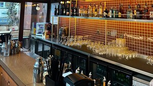 Zona de bar con estantes llenos de botellas de licor, vasos y una máquina de café.