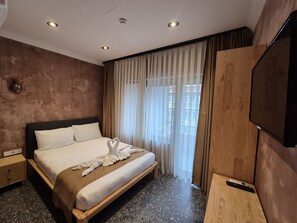 A hotel room with a bed, a TV, a wooden wardrobe, a window with curtains, and a wall-mounted light fixture. - BKM Mutfak Hostel (Istanbul)