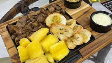 Un safata de fusta amb carn a la planxa, trossos d'ananas, pa torrat i un bol petit de salsa.