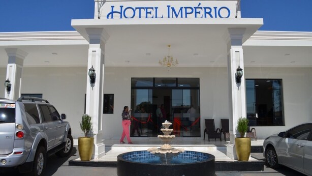 The entrance of Hotel Império with a fountain, white columns, and a clear blue sky. - Hotel Imperio (Aparecida do Taboado)