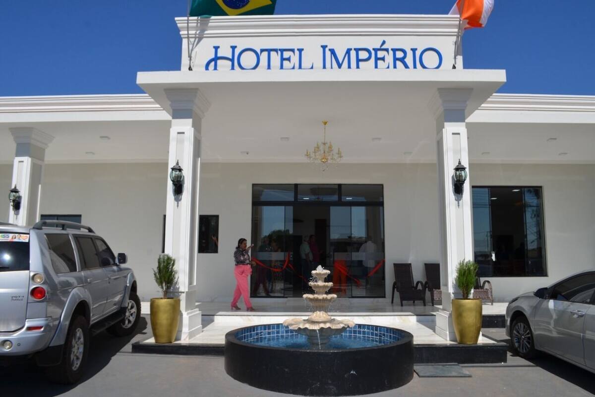 The entrance of Hotel Império with a fountain, white columns, and a clear blue sky.