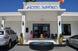 A entrada do Hotel Império com uma fonte, colunas brancas e um céu azul límpido.