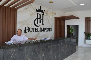 Balcão de recepção de hotel com parede de mármore, logotipo com coroa e recepcionista.