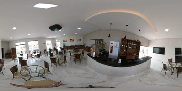 Um hall de hotel espaçoso com um balcão de recepção curvo, várias áreas de estar e um amplo espaço aberto com iluminação natural.