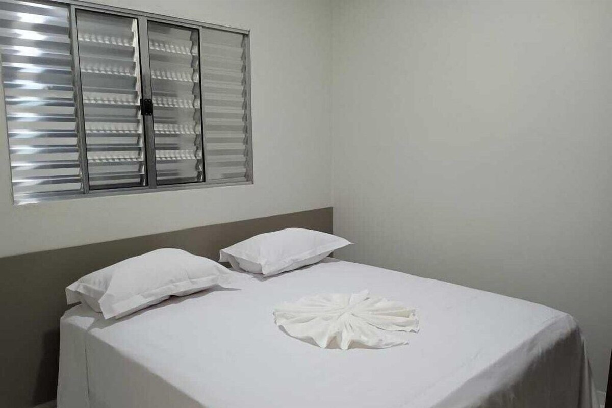Una cama individual con ropa blanca de cama y almohadas, una ventana con persianas y una pared lisa.