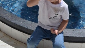 A child sitting by a pool with a fountain, wearing a white t-shirt and jeans. - Hotel Imperio (Aparecida do Taboado)