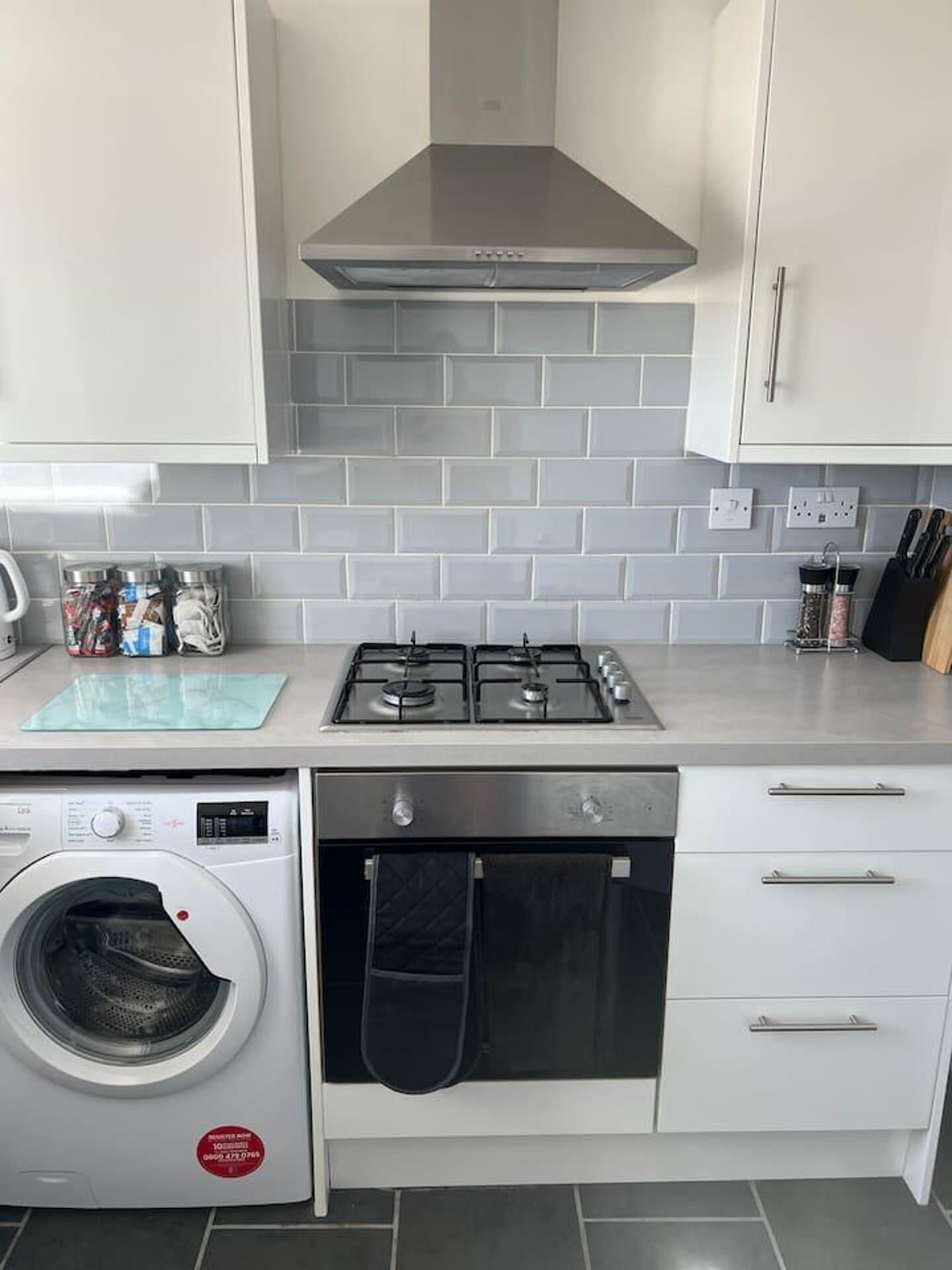 A compact kitchen with a gas stove, a built-in washing machine, and white cabinets.