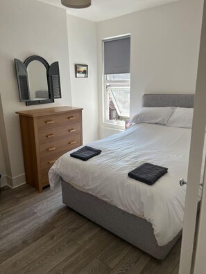 Een slaapkamer met een bed, een houten dressoir, een raam met uitzicht en een plafondlamp.