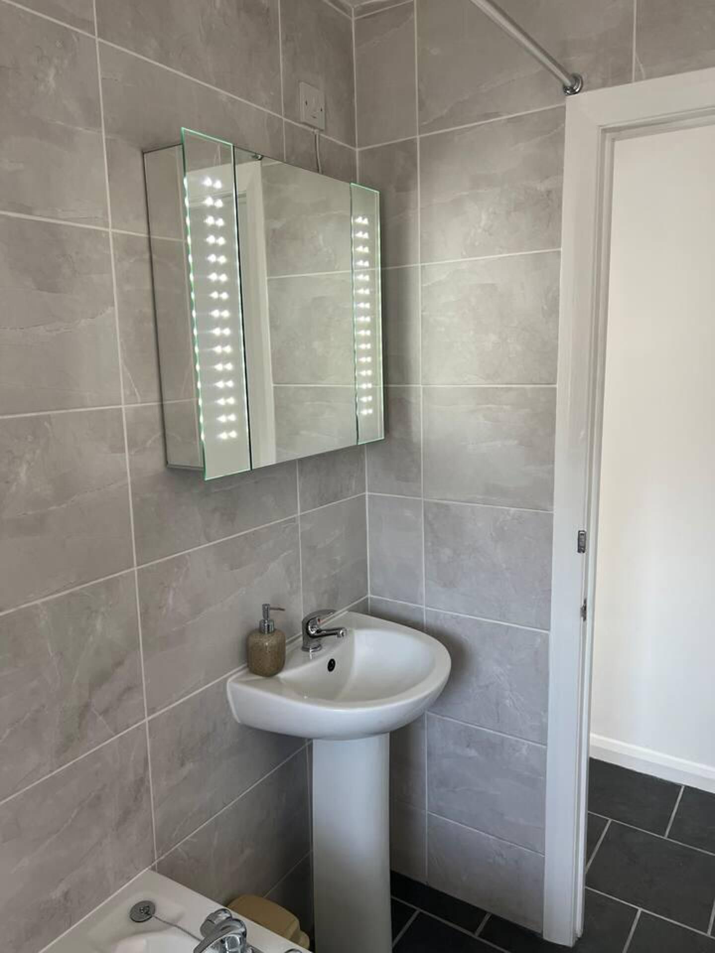 A bathroom with a white pedestal sink, a mirror with LED lights, and a door.