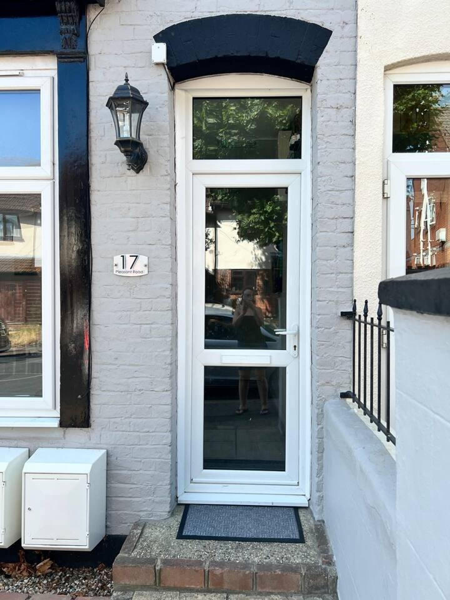 Una casa blanca con una puerta negra, un letrero con el número 17 y un farol negro en la pared.