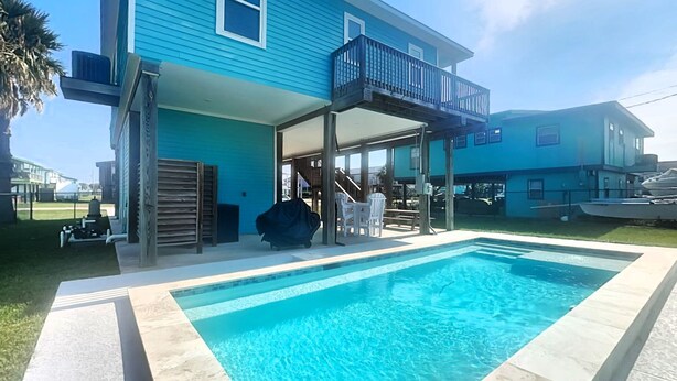 Una propiedad residencial con piscina, un patio cubierto y un edificio de dos pisos con balcón.