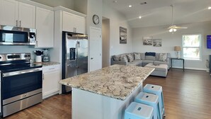 Una cocina moderna con electrodomésticos de acero inoxidable, una isla de mármol y taburetes de color azul claro.