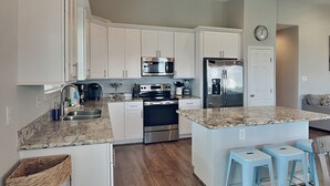 Una cocina moderna con armarios blancos, electrodomésticos de acero inoxidable, encimera de granito y una isla central con taburetes de bar.