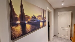 A hallway with a large painting of a bridge and boats, a white door, and a tiled floor.