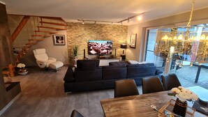 A modern living room with a black sofa, a wooden dining table, and a staircase.