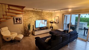 A modern living room with a stone wall, a sofa, a chair, a TV, and a staircase.