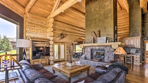 L’intérieur d’une cabane en rondins, avec une cheminée en pierre, des canapés en cuir et un téléviseur.