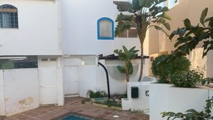 A swimming pool surrounded by white walls with a blue window and a small garden area with plants. - terraced house (Marbella)