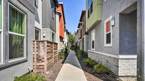 Un étroit sentier entre des immeubles résidentiels, avec une allée en béton, une clôture en bois et quelques petites plantes.