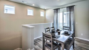 Un coin repas avec une table dressée pour quatre personnes, comprenant des assiettes, des bols et des couverts. Il y a quatre chaises, une fenêtre avec des rideaux et un plafond doté d’un éclairage encastré.