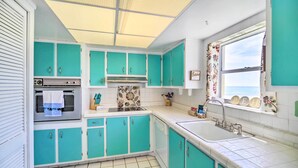 Een keuken met blauwgroene kastjes, een roestvrijstalen oven en een raam met decoratieve gordijnen.