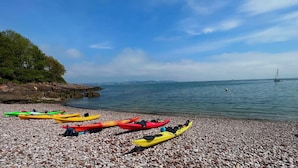 A pebbled beach with kayaks lined up and a sailboat in the distance. - Hot Tub Heaven in Beautiful Village, Close to Beaches - Blue Flag & Dog Friendly (Stoke Gabriel)