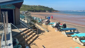 A wooden deck with picnic tables and chairs, overlooking a beach. - Hot Tub Heaven in Beautiful Village, Close to Beaches - Blue Flag & Dog Friendly (Stoke Gabriel)
