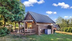 Eine Holzhütte mit Veranda, einem kleinen angebauten Schuppen und einem eingezäunten Garten.