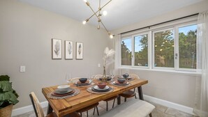 A dining area with a wooden table set for six, surrounded by chairs, a vase with feathers, and framed artwork on the wall. - Funky MINI GOLF Home filled with Amenities (Gainesville)