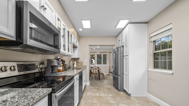 A modern kitchen with stainless steel appliances, granite countertops, and a tiled floor. - Funky MINI GOLF Home filled with Amenities (Gainesville)