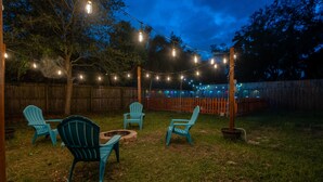 A backyard with string lights, a wooden fence, and four blue Adirondack chairs. - Funky MINI GOLF Home filled with Amenities (Gainesville)