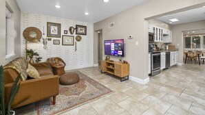 A spacious living room with a brown leather sofa, a patterned rug, and a television displaying streaming services. - Funky MINI GOLF Home filled with Amenities (Gainesville)