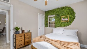 A bedroom with a bed, a wooden dresser, a ceiling fan, and a wall with a green leafy design. - Funky MINI GOLF Home filled with Amenities (Gainesville)