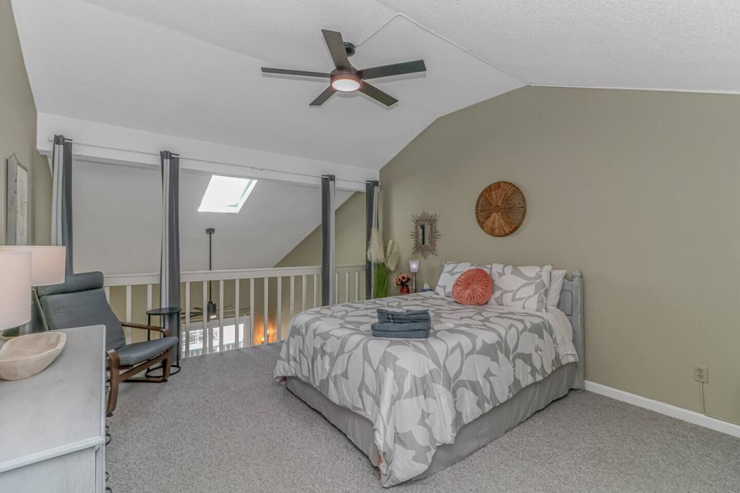 A bedroom with a bed, a ceiling fan, a skylight, and a view of the outside.