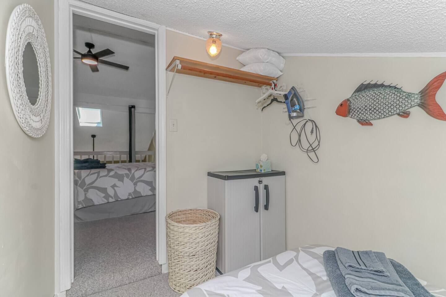 A bedroom with a bed, a small cabinet, a wicker basket, a ceiling fan, and a fish decoration.