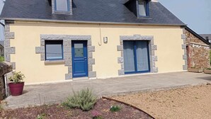 Kaksikerroksinen talo, jossa on kiviverhous, kaksi sinistä ovea ja pieni puutarha-alue edessä.