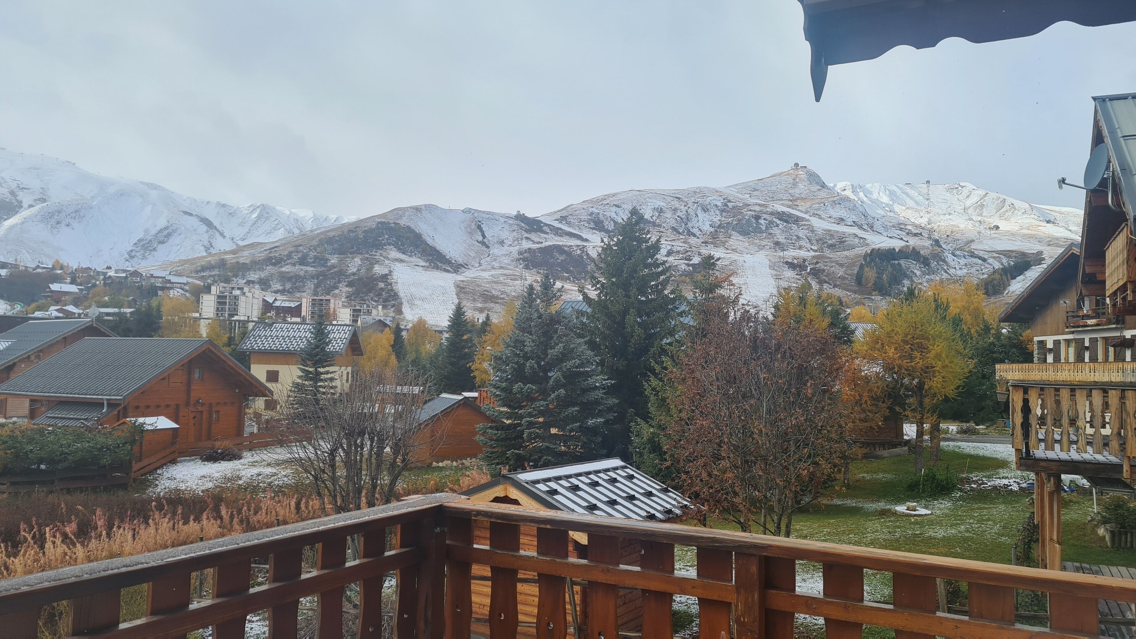 Una baita di legno con tetto spiovente, circondata da montagne innevate e alberi dai colori autunnali.